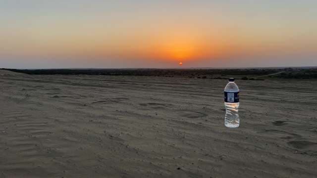 Desert Sunset With Water Bottle on Sandy Landscape
