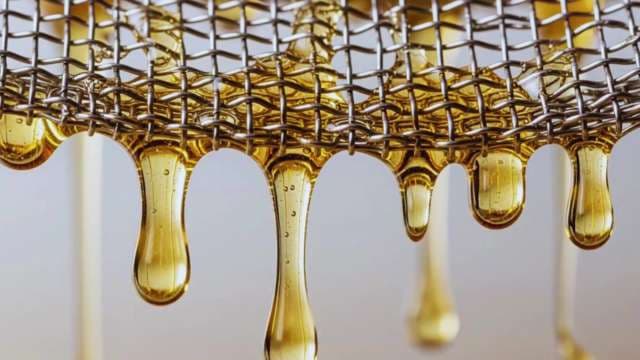 Macro Golden Liquid Dripping Through Metal Mesh Sieve