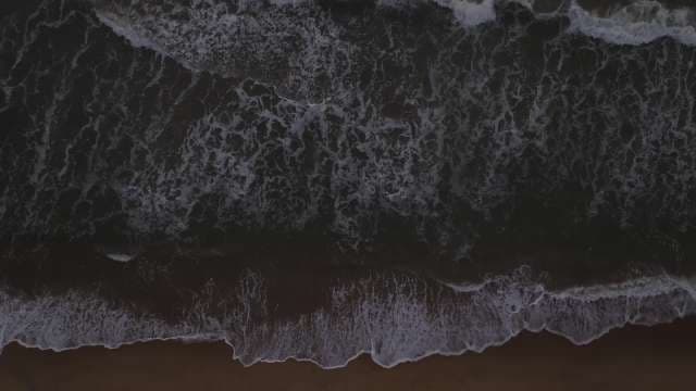 Aerial Top-Down View of Ocean Waves Crashing on Dark Sand Beach
