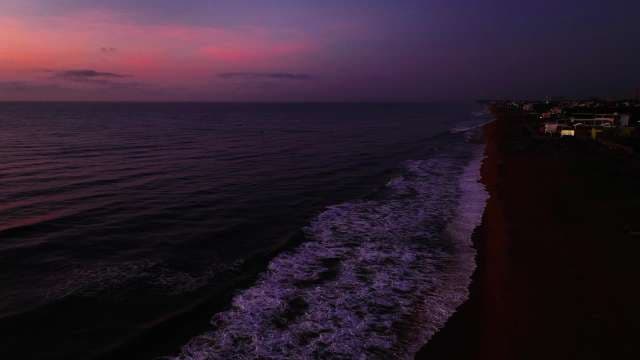 Aerial View of Ocean Waves Hitting Dark Shore at Purple Sunset