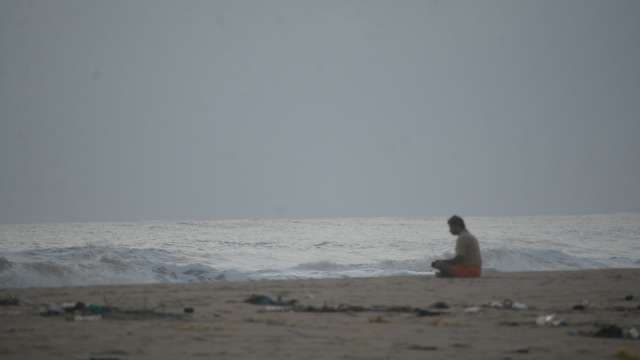 Man Sitting Alone on Cloudy Beach Watching Ocean Waves