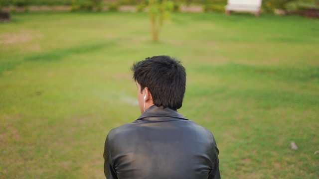 Young Man in Leather Jacket Sitting in Park Listening to Music
