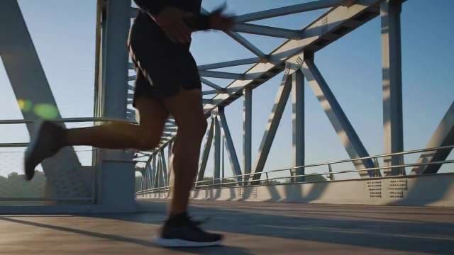 Man Jogging Across Modern Steel Bridge at Sunrise