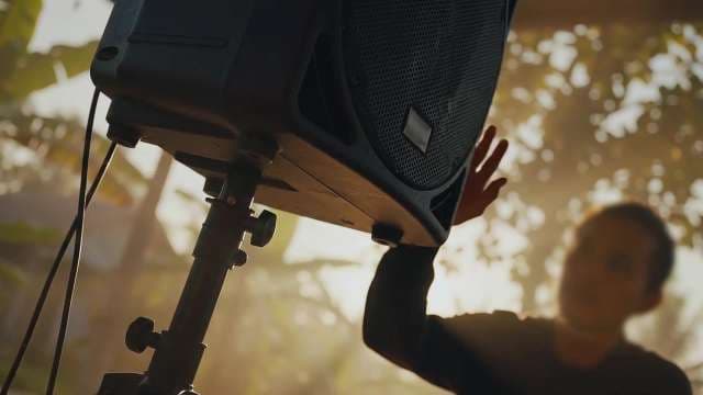 Man Adjusting Professional Audio Speaker Outdoors in Tropical Sunlight