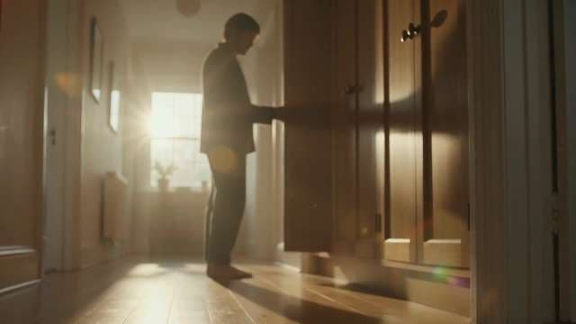 Man Opening Wardrobe in Sunny Hallway During Morning