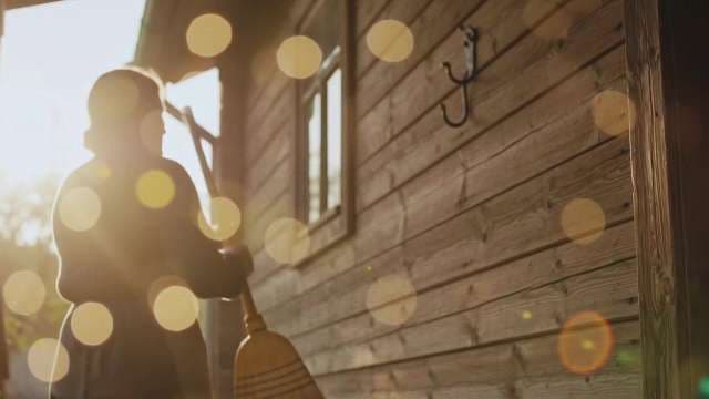 Silhouette of Woman Sweeping Porch of Rustic Wooden Cabin at Sunset