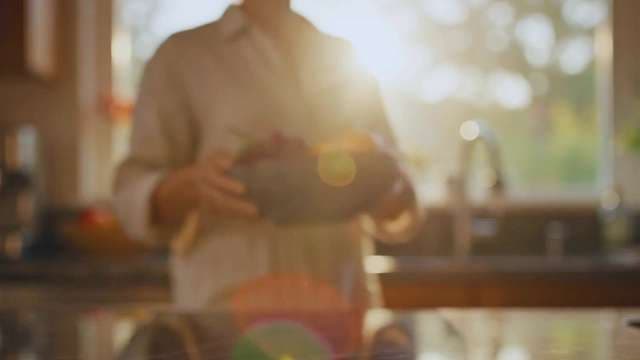 Sunlit Person Carrying Fresh Fruit Bowl in Warm Kitchen Setting