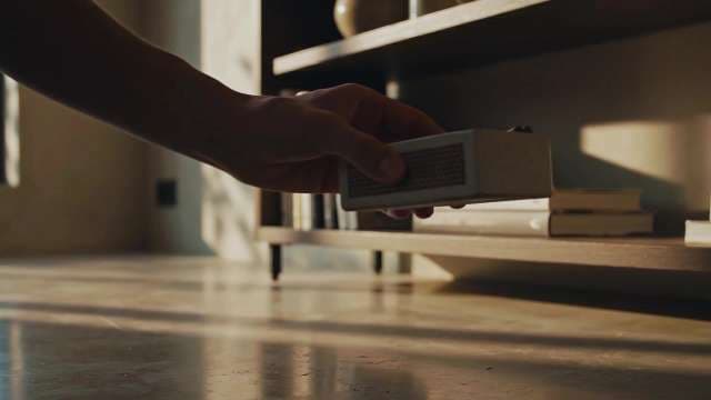 Hand Picking Up Portable Speaker in Warm Sunset Interior