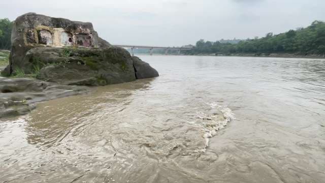 Murky River Flowing Past Ancient Rock Carvings and Bridge