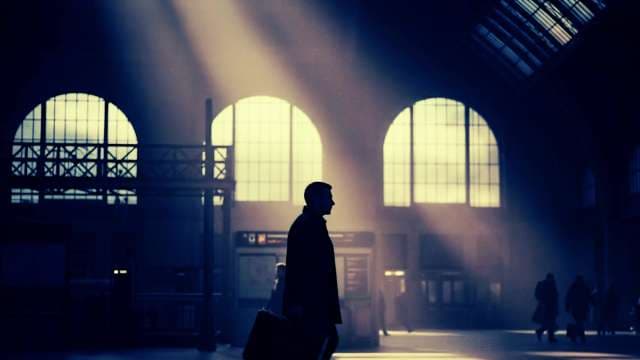 Silhouette of Traveler Walking Through Sunlit Train Station Hall