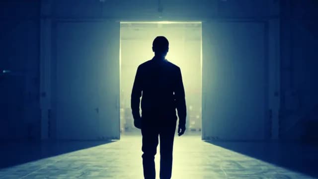 Silhouette of Man Walking Toward Bright Warehouse Doorway
