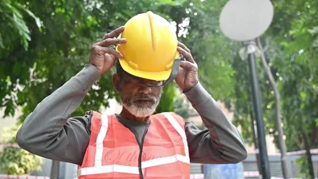 Senior Construction Worker Putting On Yellow Hard Hat Outdoors