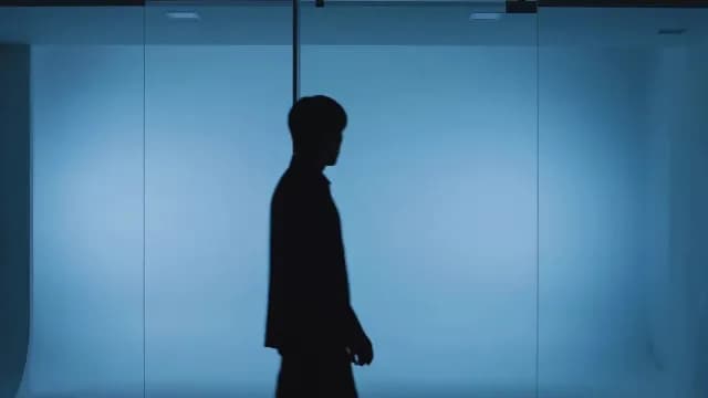 Silhouette of Businessman Walking Past Blue Glass Wall