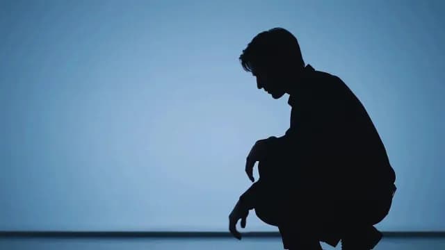 Silhouette of Depressed Man Crouching on Blue Background