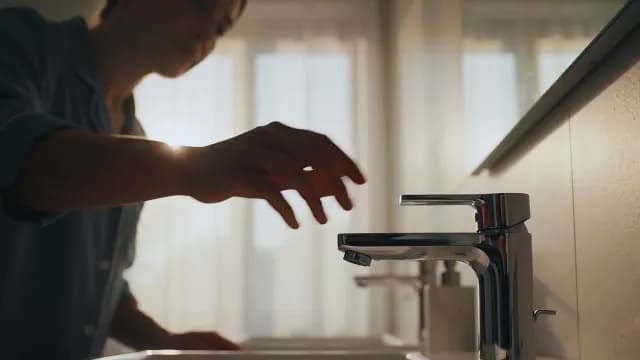 Woman Reaching to Turn on Modern Bathroom Sink Faucet at Sunrise