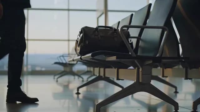 Man Picking a Black Leather Travel Bag from Airport Terminal Seating