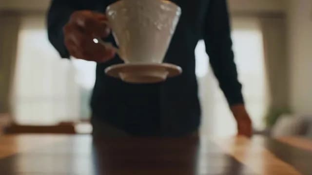 Man Placing Elegant White Tea Cup on Wooden Table Indoors