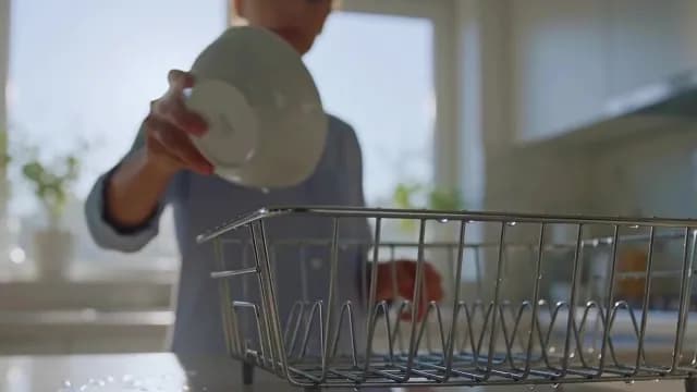 Woman Placing Clean White Bowl into Wire Drying Rack in Kitchen