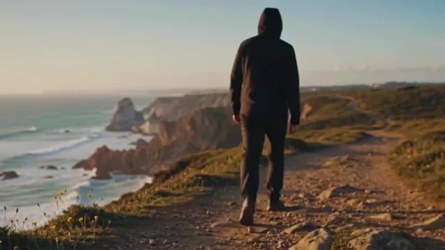 Man in black hoodie walking scenic coastal cliffs at sunset