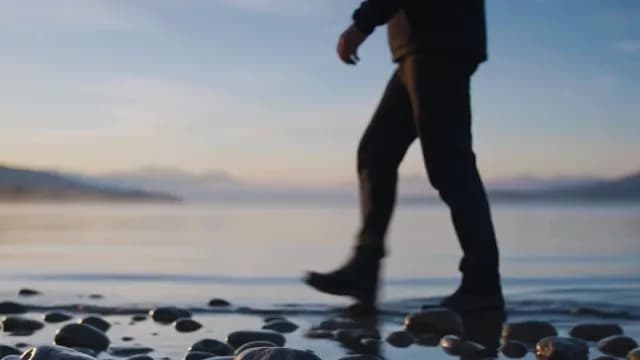 Person Walking Along Calm Shoreline at Sunset