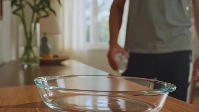 Man Pouring Ice Cubes in a Glass Baking Dish on Wooden Kitchen Countertop