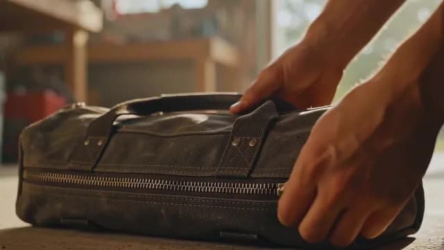 Hands Zipping Canvas Tool Bag in Sunlit Workshop