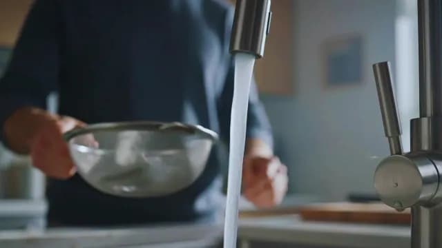 Person Rinsing Ingredients with Water in Modern Kitchen Sink