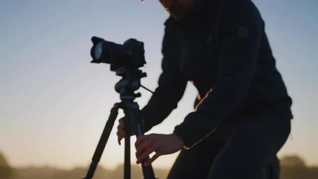 Photographer Adjusting Professional DSLR Camera on Tripod at Golden Hour