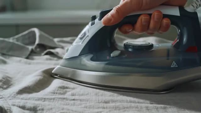 Person Ironing Wrinkled Linen Shirt with Modern Steam Iron