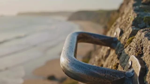 Metal safety handrail on rugged coastal cliff overlooking ocean beach
