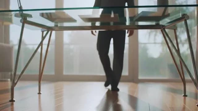 Professional Walking Toward Modern Glass Desk in Sunlit Minimalist Office