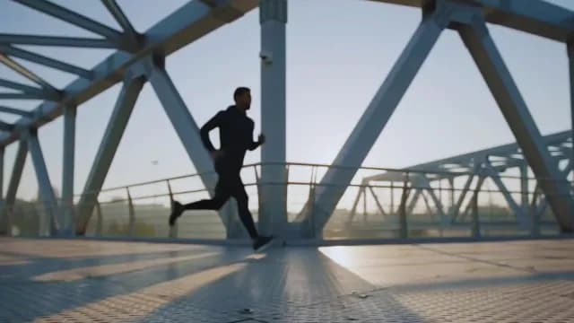 Man Jogging Across Modern Urban Bridge at Sunrise