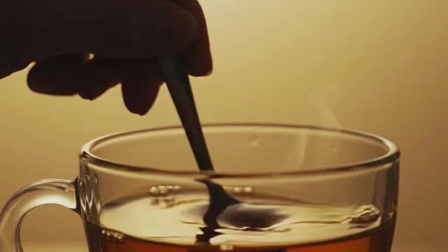 Stirring Hot Tea in Glass Mug with Rising Steam