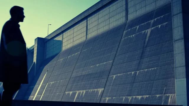 Silhouetted Man Walking Past Massive Concrete Industrial Dam
