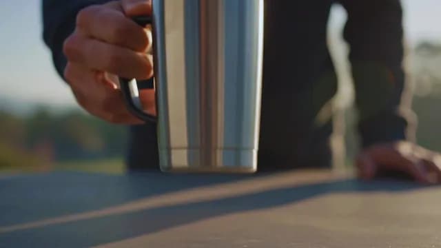 Man Placing Stainless Steel Coffee Mug on Outdoor Table at Sunset