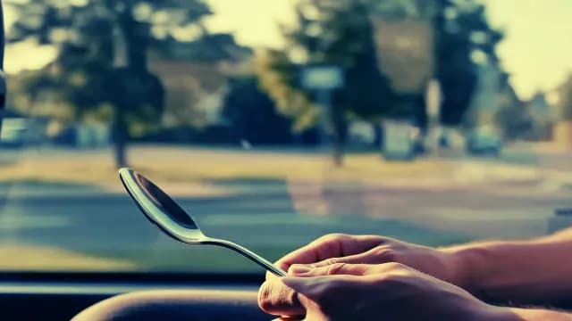 Hands Holding a Silver Spoon Against a Blurred Urban Background