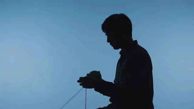 Silhouette of Man Winding Yarn Ball on Blue Background