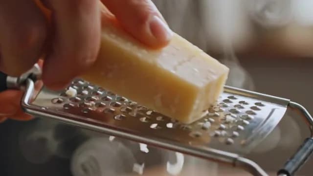 Close-Up of Grating Fresh Parmesan Cheese Over Steaming Dish