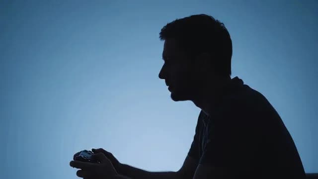 Silhouette of Male Gamer Holding Controller Against Blue Background