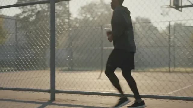 Athletic Man Running Past Basketball Court Fence at Sunrise