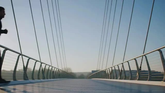 Man Jogging on Modern Pedestrian Bridge in Daylight
