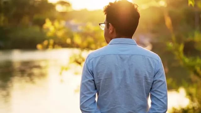 Young Man Gazing at Lake During Golden Hour Sunset