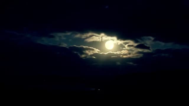 Full Moon Glowing Through Dark Clouds in Night Sky