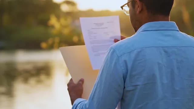 Man Reviewing Business Documents Outdoors at Sunset Near Lake
