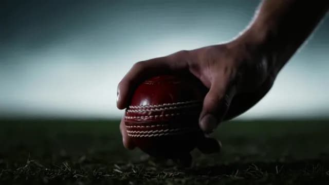 Close Up of a Hand Placing a Red Cricket Ball on Grass