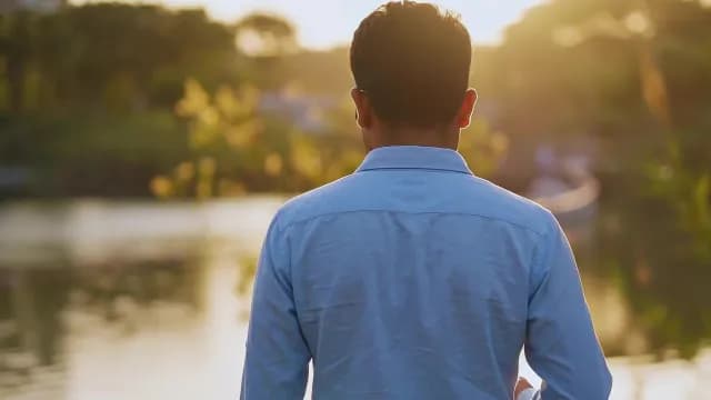 Man in Blue Shirt Watching Golden Sunset Over Tranquil River