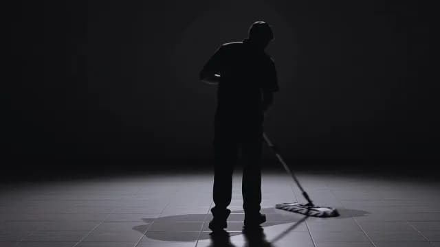 Silhouette of Male Janitor Mopping Tiled Floor in Dramatic Light