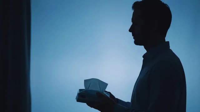 Silhouette of Man Holding Tissue Box Against Blue Background