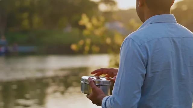 Man Holding Metal Lunch Box Outdoors During Golden Hour