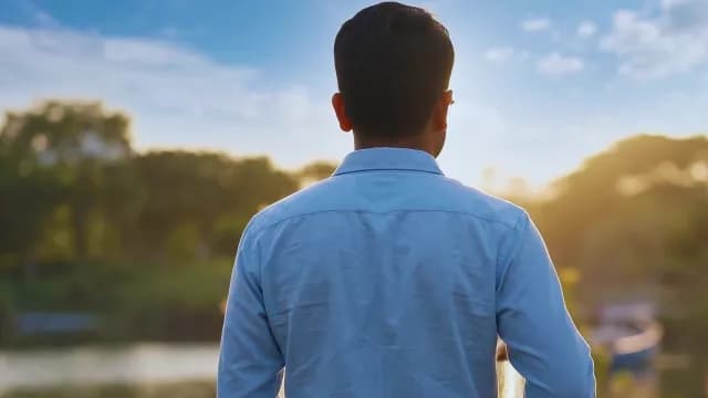 Young Man Watching the Sunrise Over a Park and River